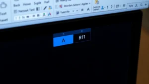 Close-up overhead view of computer monitor displaying Excel spreadsheet with cells A1 and B1 selected and highlighted in blue, showing merge buttons in the Home ribbon toolbar at top of screen