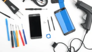 Organized workspace with precision screwdrivers, plastic spudgers, tweezers, anti-static wrist strap, and heat gun laid out on clean white surface next to open Samsung smartphone