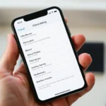Person holding iPhone showing iCloud backup settings screen with recovery options visible, natural lighting, clean desk background, focused on device display