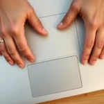 Close-up overhead view of hands positioned on a silver Chromebook trackpad, fingers demonstrating two-finger tap gesture with clear finger placement visible