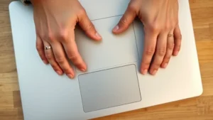 Close-up overhead view of hands positioned on a silver Chromebook trackpad, fingers demonstrating two-finger tap gesture with clear finger placement visible